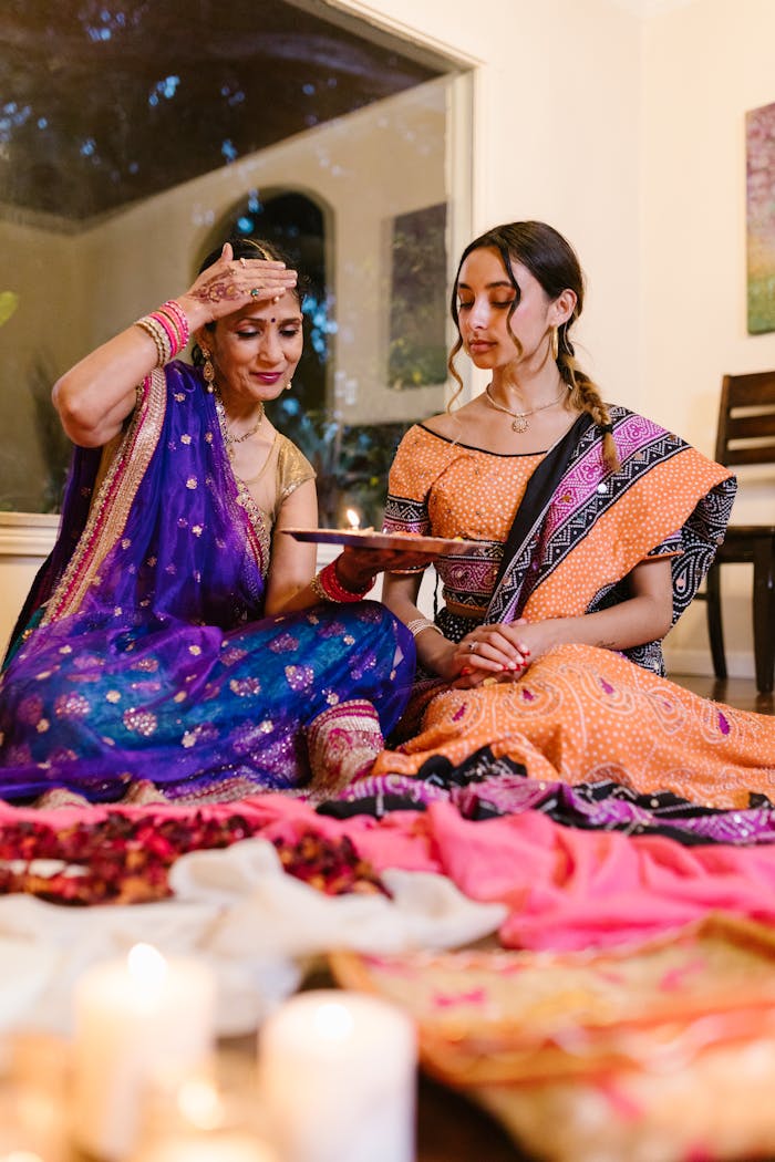 Contact Two women in vibrant sarees celebrating Diwali indoors, showcasing traditional Indian culture.