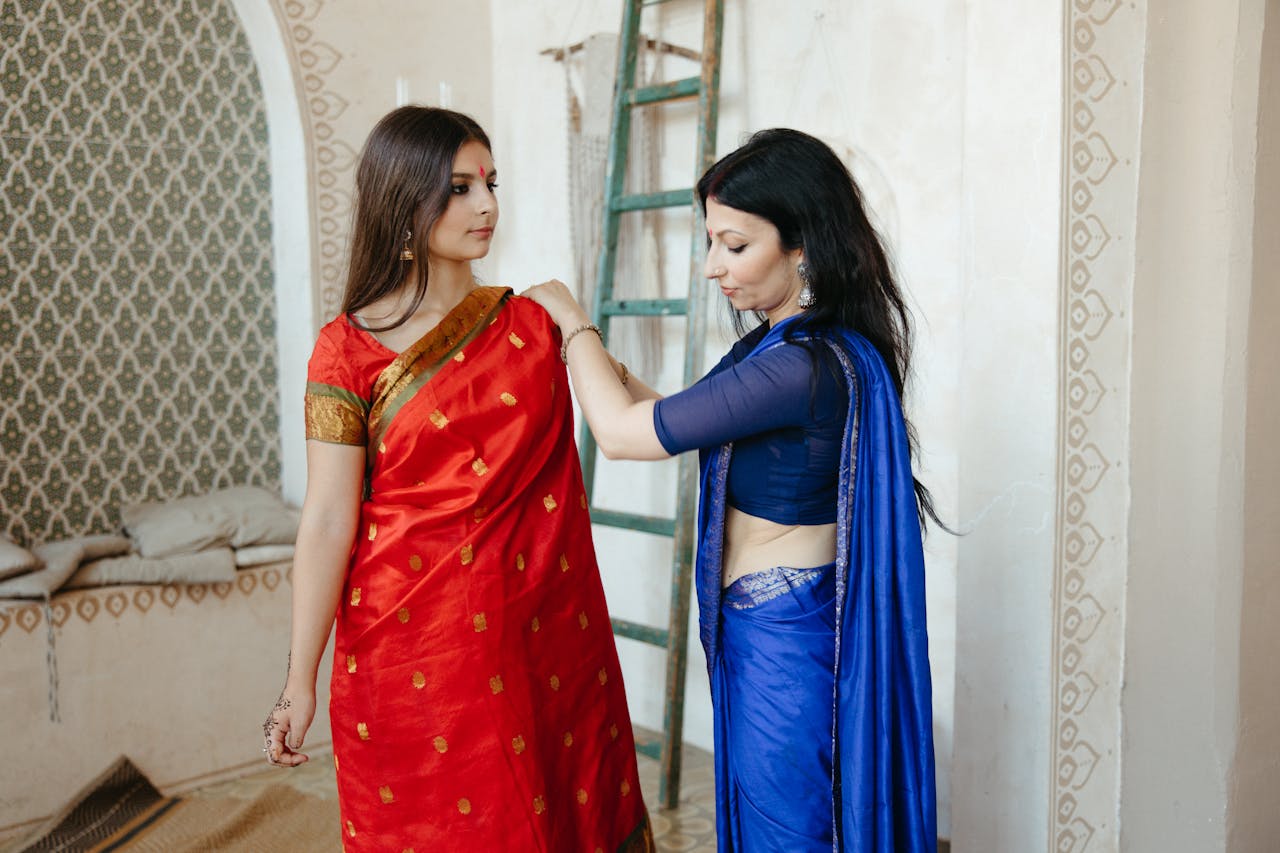 Crafting Captivating Headlines: Your awesome post title goes here Two South Asian women wearing traditional sarees and preparing indoors.