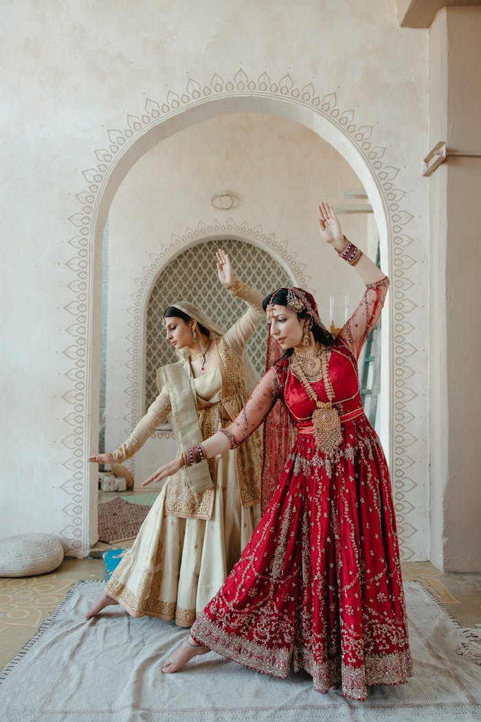 Home Two women in vibrant saris perform a traditional Indian dance indoors.